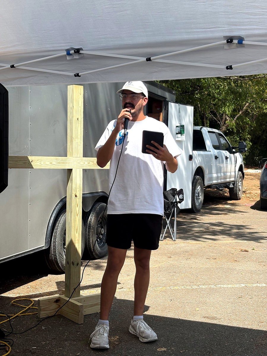 A volunteer speaking into a microphone beside a wooden cross